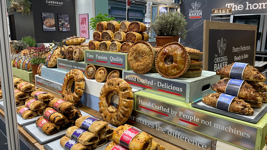 A display stand at the Farm Shop and Deli Show featuring a selection of baked products including savoury pies, deli rolls and sausage rolls.